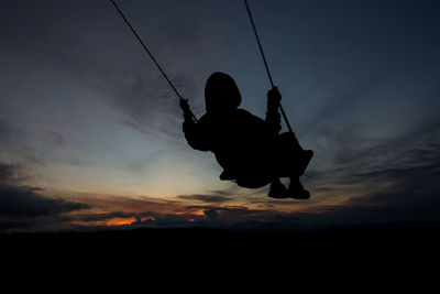 Low angle view of man swinging against sky during sunset