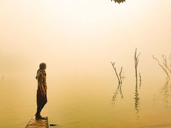 Man standing in lake against sky during sunset