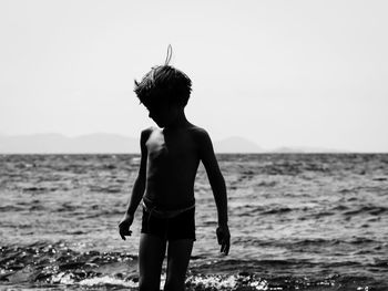 Shirtless man standing at beach against clear sky on sunny day