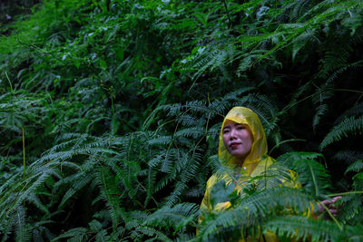 Portrait of woman wearing raincoat while standing amidst plants during rainy season