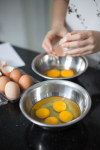 Midsection of woman breaking eggs in kitchen