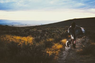 Woman with dog walking on field against sky