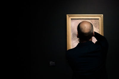 Rear view of man putting picture frame on wall