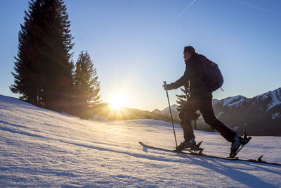 Side view of mature man skiing on snow covered landscape against blue sky during sunset