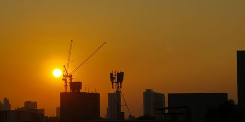 Silhouette cranes at construction site during sunset