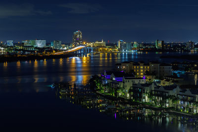 Illuminated bridge over river by buildings against sky at night