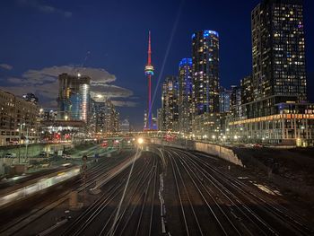 Illuminated railroad tracks amidst buildings in city at night