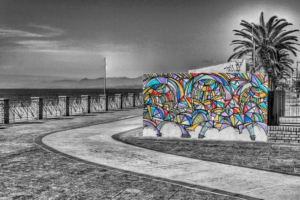 art, creativity, art and craft, multi colored, graffiti, built structure, blue, sky, architecture, outdoors, road, no people, railing, day, palm tree, street, building exterior, wall - building feature, sidewalk, absence