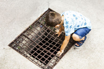 High angle view of boy looking through metal grate on road