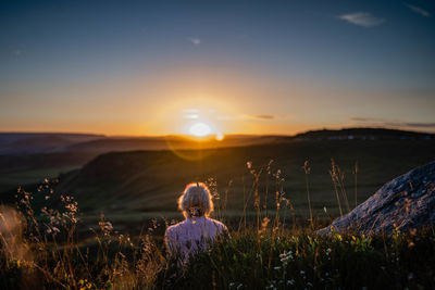 Rear view of woman standing on field against sky during sunset