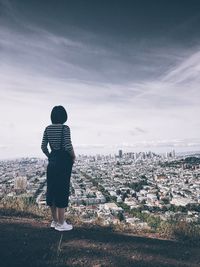 Rear view of woman standing by cityscape against sky