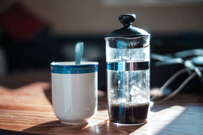 Close-up of french press by mug on table