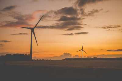 Silhouette wind turbines on field against sky during sunset