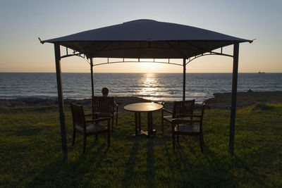 Chairs on beach against clear sky at sunset