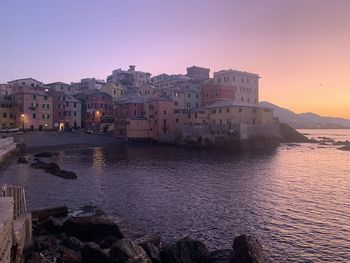 Buildings by sea against clear sky at sunset