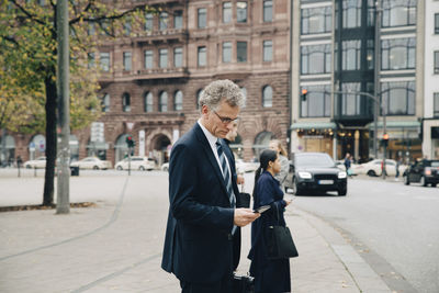 Side view of mature businessman using smart phone while standing in city