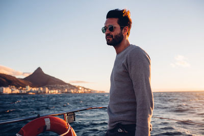 Young man wearing sunglasses on beach against sky during sunset