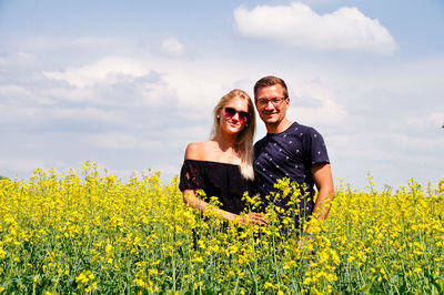 Portrait of couple standing amidst yellow flowers on oilseed rape field