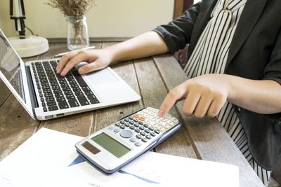 Midsection of businesswoman using calculator and laptop at office