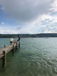 People sitting on pier over sea against sky