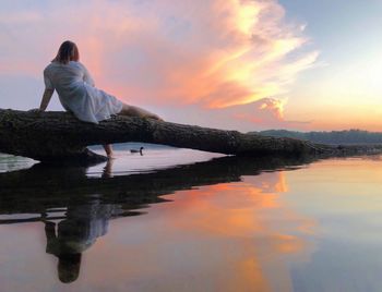 Woman looking at lake against sky during sunset