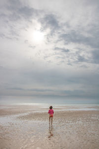 Rear view of woman standing on beach against sky