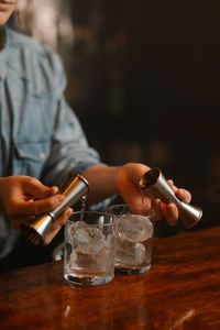 Crop unrecognizable barkeeper pouring alcohol drinks from jiggers into glasses with ice cubes while preparing cocktails at car counter on blurred background