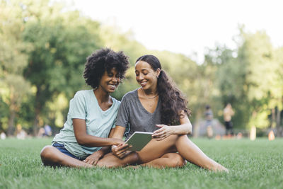 Happy young woman using phone while sitting on grass