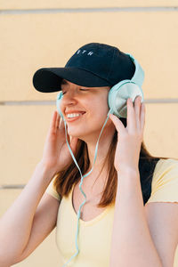 Young woman with mint headphones and black cap outside on the street.