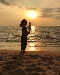 Silhouette woman standing on beach against sky during sunset