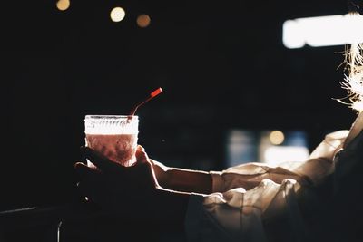 Close-up of hand holding illuminated lighting equipment against black background