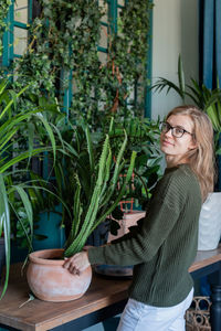 Young woman in green sweater taking care of the plants at home