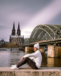 Man sitting on bridge over river against sky