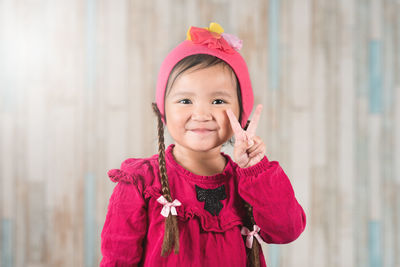 Portrait of smiling girl gesturing while standing against wall