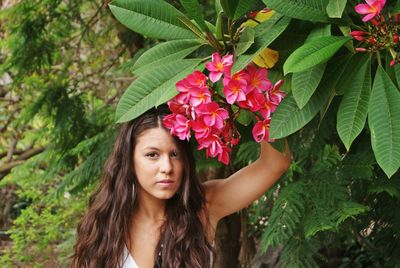 Portrait of young woman touching flowers growing at park