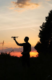 Silhouette men standing against sky during sunset with a drone in his hand