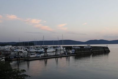 Sailboats moored in harbor against sky during sunset