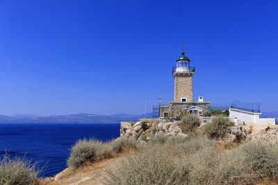 Lighthouse amidst sea and buildings against clear blue sky