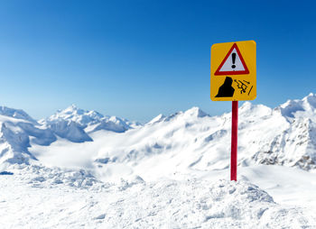 Road sign on snow covered mountain against clear blue sky
