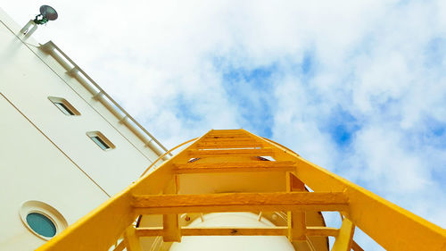 Low angle view of yellow vertical ladder against sky