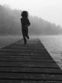 Full length of boy running on pier over river during foggy weather