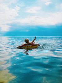 Woman on inflatable ring in sea against cloudy sky