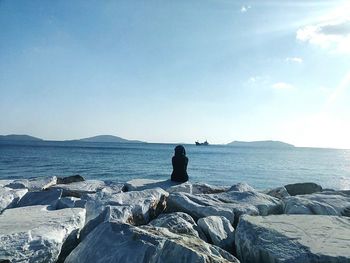 Rear view of woman sitting on rock by sea against clear sky