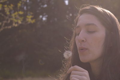 Close-up of beautiful young woman blowing dandelion