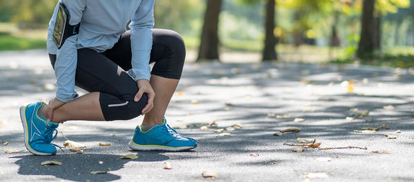 Low section of woman touching ankle and knee in pain on road