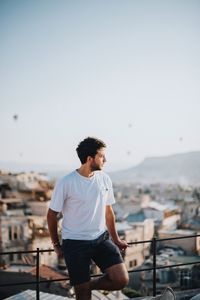 Young man looking at cityscape against sky