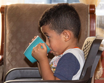 Sitting child drinking food in a cup