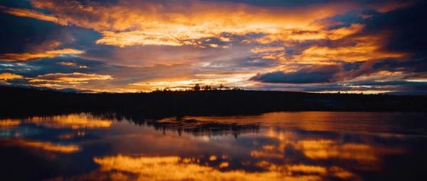 Scenic view of lake against dramatic sky during sunset