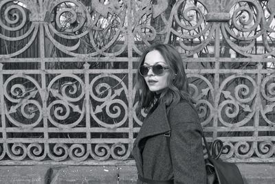 Side view close-up of woman wearing sunglasses while standing by fence