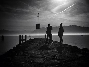 Rear view of woman standing on pier at sunset